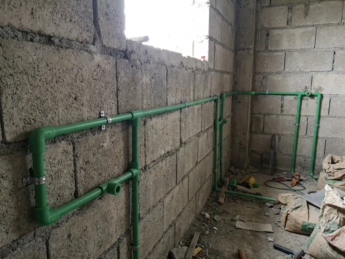 Green PPR water pipes with heat-fused fittings on a bare wall