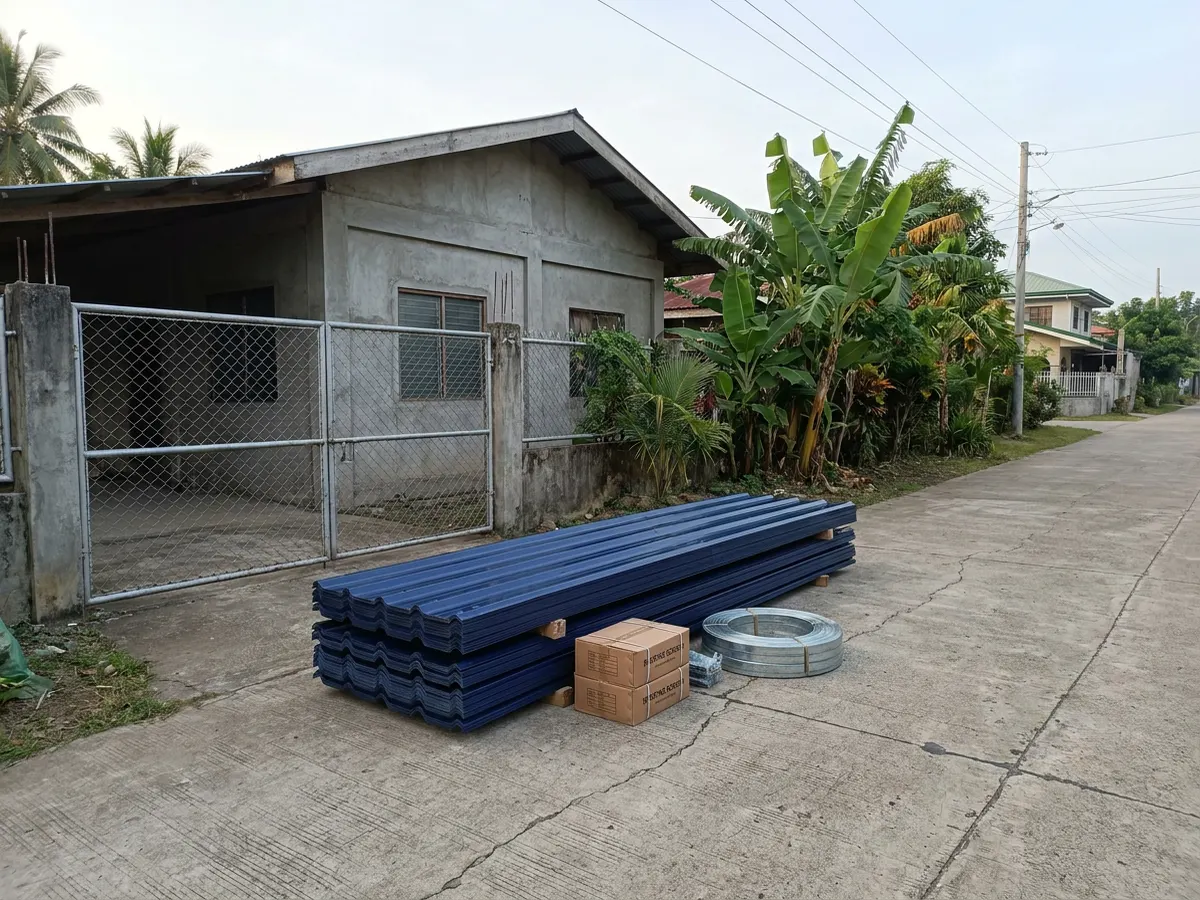 New blue long-span roofing sheets and boxes of screws stacked in front of a house, ready to count