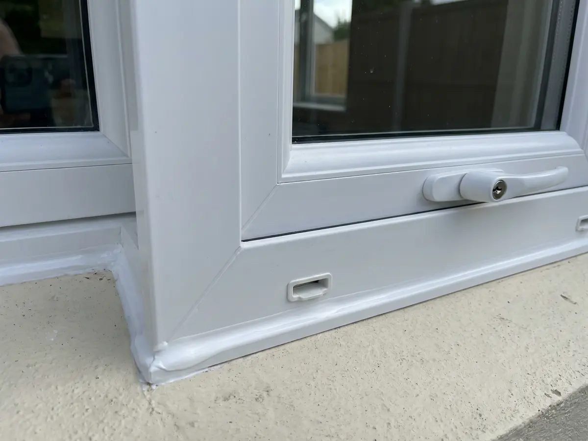 Corner of a white uPVC window with a neat sealant line against the wall
